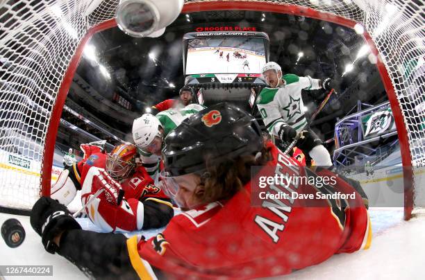 Radek Faksa of the Dallas Stars falls into goaltender Cam Talbot of the Calgary Flames as Rasmus Andersson reaches to try and stop the puckafter...