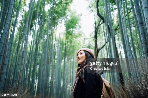 beautiful young asian female backpacker enjoying in nature. she is walking along the pathway in the bamboo grove of arashiyama, kyoto, exploring and enjoying the spectacular nature scenics - bambusnår bildbanksfoton och bilder