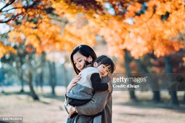 a loving young asian mother embracing adorable little daughter in arms, spending time together and enjoying the beautiful autumn scenics in nature park on a beautiful sunny day - korea japan stock pictures, royalty-free photos & images