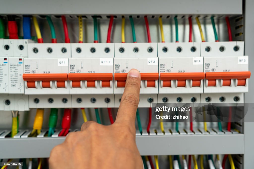 Human hand is flipping the power switch in the electrical control cabinet