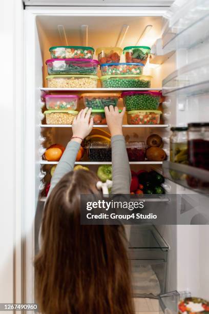 mädchen, das rohkost aus dem kühlschrank nimmt - full fridge stock-fotos und bilder