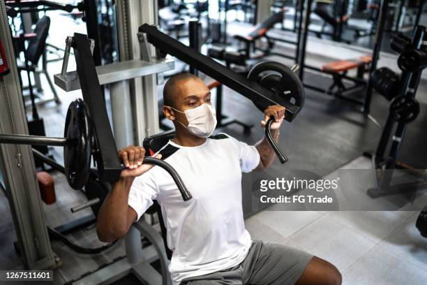 man doing strength workout exercise in gym with face mask - health club stock pictures, royalty-free photos & images