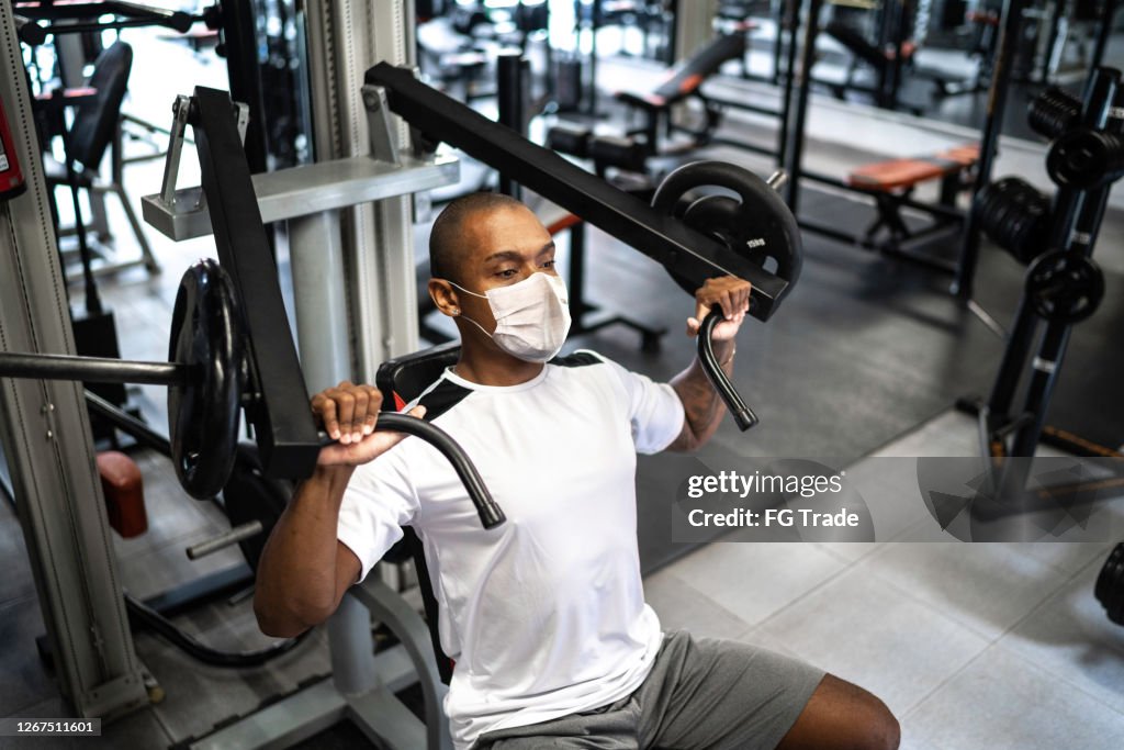 Man doing strength workout exercise in gym with face mask