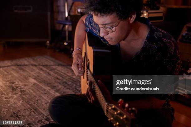 mixed-race young man playing acoustic guitar sitting on floor in music studio - songwriter stock pictures, royalty-free photos & images