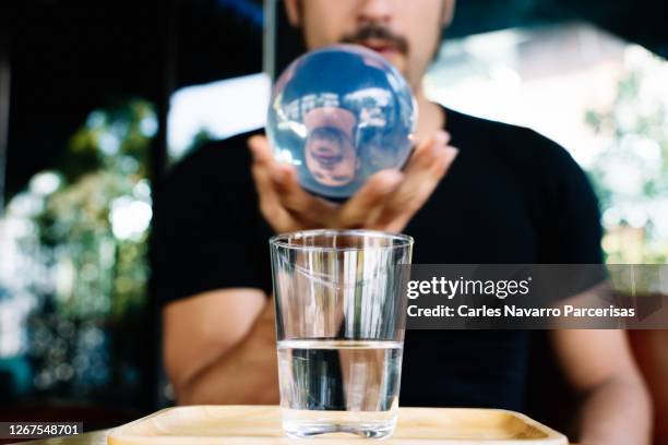 selective focus on a man's hand with a crystal ball on top of a glass filled with water - crystal ball stock-fotos und bilder