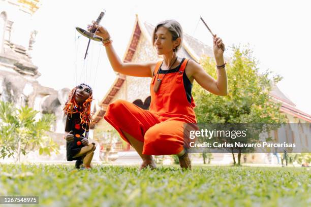 woman dressed in an orange jumpsuit manipulating a puppet with the figure of a woman in front of a buddhist temple - puppeteer photos et images de collection