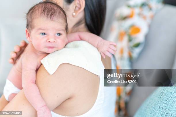 latina mutter hält neugeborenes baby über die schulter zu hause - burping stock-fotos und bilder