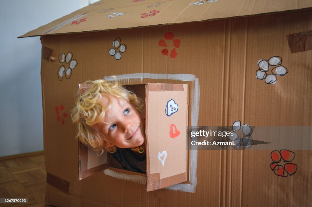 Caucasian boy looking through window of cardboard house