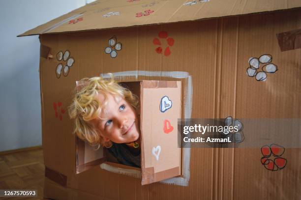 caucasian boy looking through window of cardboard house - playhouse stock pictures, royalty-free photos & images