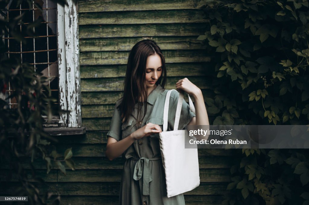 Young beautiful woman in a green dress looks into a white eco bag