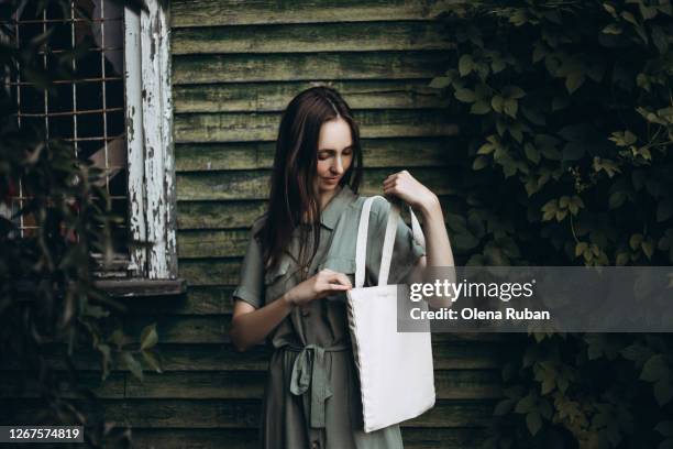 young beautiful woman in a green dress looks into a white eco bag - cloth bag stock pictures, royalty-free photos & images