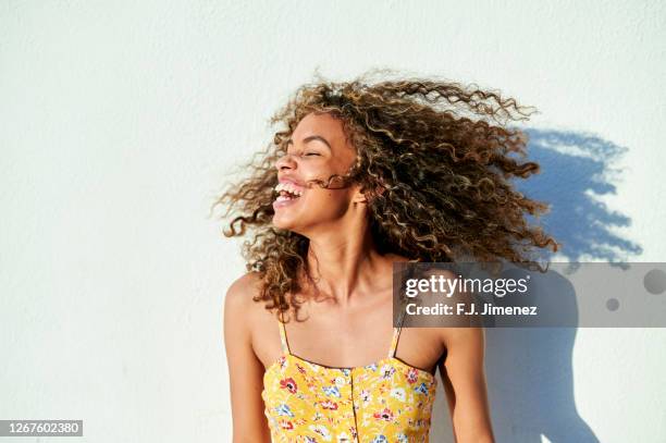 portrait of woman moving her hair in front of white wall - robe jaune photos et images de collection