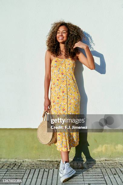 woman with afro hair in front of white wall - yellow dress stock-fotos und bilder