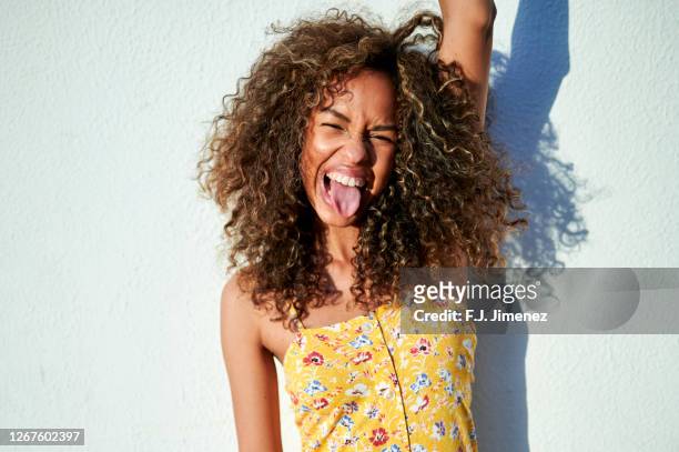 portrait of woman sticking out tongue in front of white wall - sticking out tongue stock pictures, royalty-free photos & images
