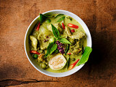 Famous internationally renowned Thai green coconut curry 'Gaeng Keow Wan Gai', with chicken in a bowl set on an old worn wooden background.