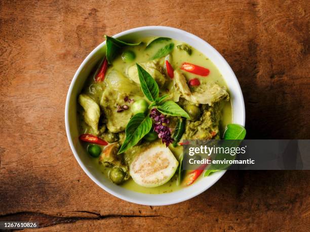 famous internationally renowned thai green coconut curry 'gaeng keow wan gai', with chicken in a bowl set on an old worn wooden background. - thai plate stock pictures, royalty-free photos & images