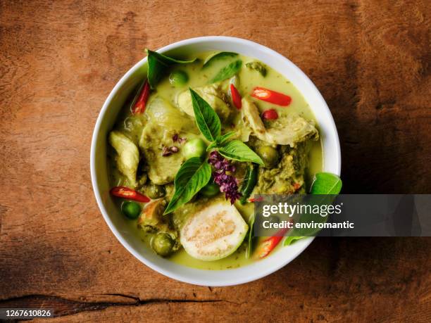 famous internationally renowned thai green coconut curry 'gaeng keow wan gai', with chicken in a bowl set on an old worn wooden background. - curry stock pictures, royalty-free photos & images