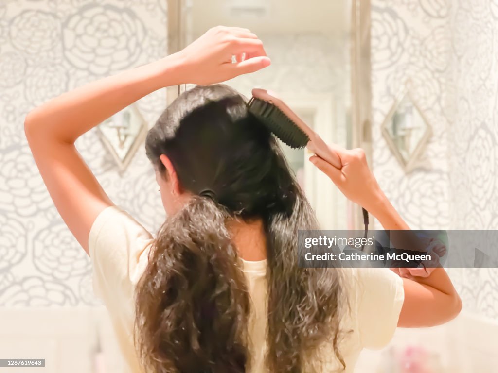 Mixed-race teen girl straightening long hair with heated hair brush