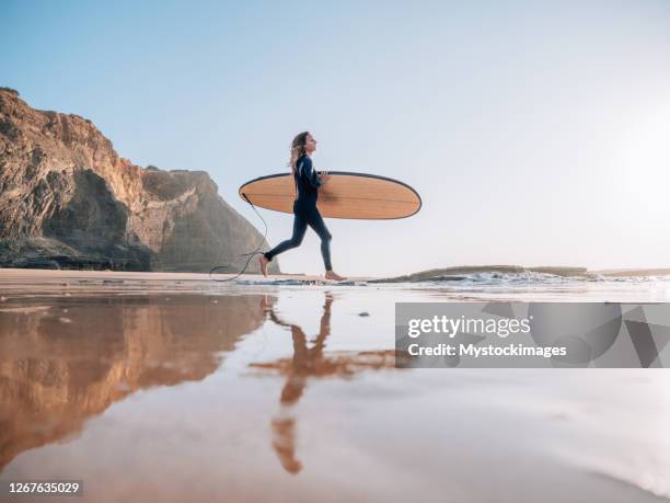 la donna surfista corre sulla spiaggia all'alba pronta per una sessione mattutina - waves crashing foto e immagini stock