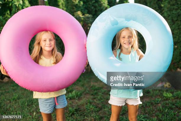porträt von zwei blonden zwillingsschwestern mit einem aufblasbaren ring - free tiny girls stock-fotos und bilder