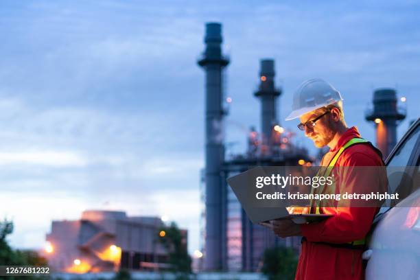 engineer wearing safety helmet using laptop with oil refinery background - gas engineer stockfoto's en -beelden