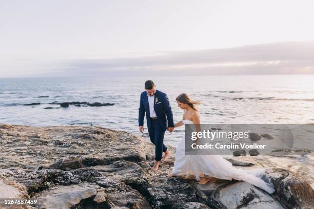 young adult couple in wedding dress and suit walking on the cliffs on the coast of porto, portugal - destination wedding imagens e fotografias de stock