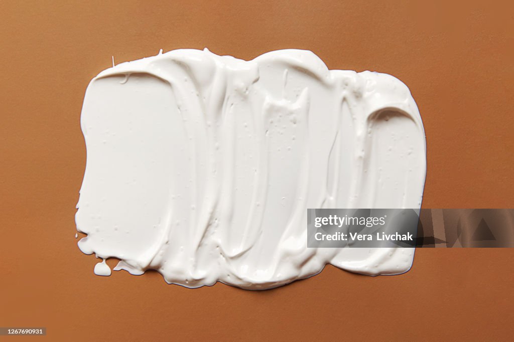 White smear of cream or oil on a pastel beige background. Flat lay style.