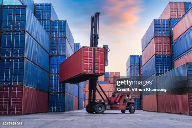 industrial container yard for logistic import export business, forklift truck handling cargo shipping container box in logistic shipping yard with cargo container stack, crane lifting up container in yard - récipient photos et images de collection