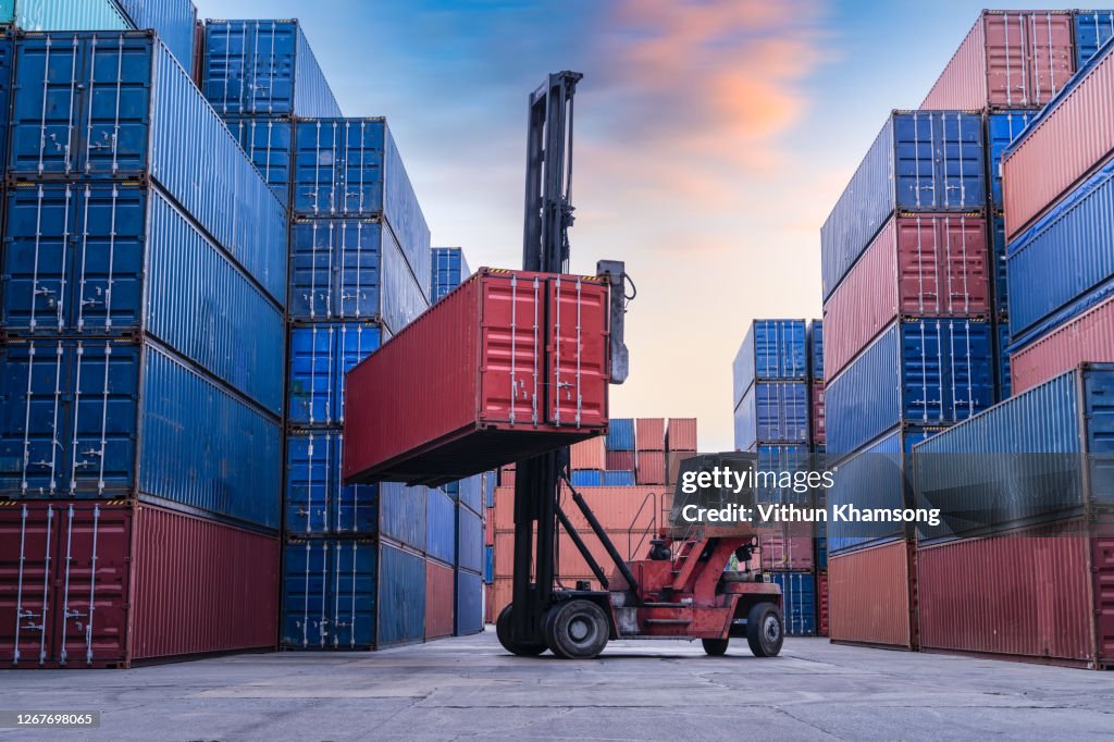 Industrial Container yard for Logistic Import Export business, Forklift truck handling cargo shipping container box in logistic shipping yard with cargo container stack, Crane lifting up container in yard