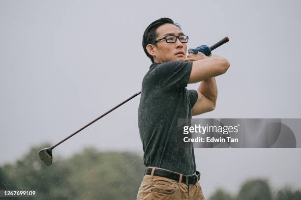 asiático chinês golfista masculino jogando golfe na chuva em melaka sozinho tee molhado fora swing - figura masculina - fotografias e filmes do acervo