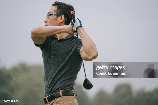 asian chinese male golfer playing golf in the rain in melaka alone wet tee off swing - man swinging golf club stock pictures, royalty-free photos & images