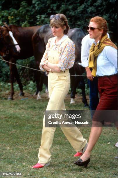 Lady Diana Spencer, wearing yellow dungarees with a floral blouse and red wedges, and Sarah Ferguson attend a polo match at Cowdray Park Polo Club in...