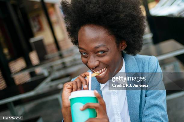 portrait of young woman eating fries and drinking a soda - cultura afro americana stock-fotos und bilder