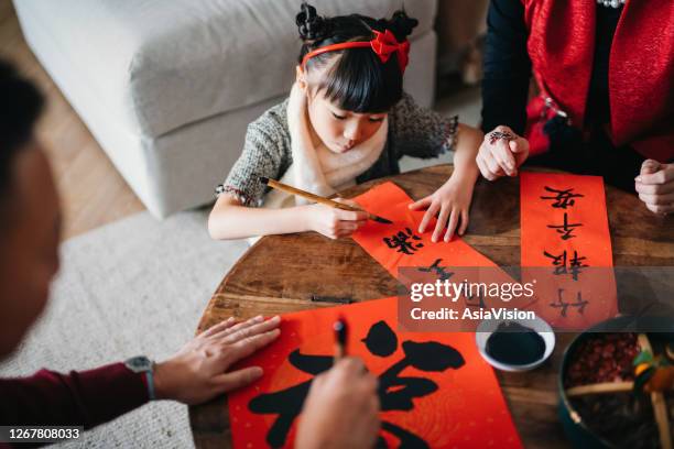 旧正月ファイチュン(縁起の良いメッセージ)のために中国の書道を練習し、自宅でカップルにそれを書くことによって孫娘を教える祖父母 - 中国語 ストックフォトと画像