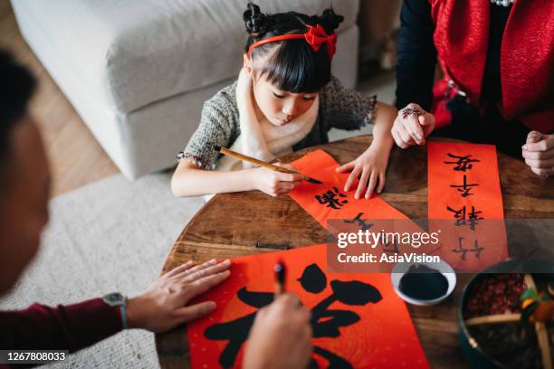 grandparents practising chinese calligraphy for chinese new year fai chun (auspicious messages) and teaching their granddaughter by writing it on couplets at home - chinês imagens e fotografias de stock