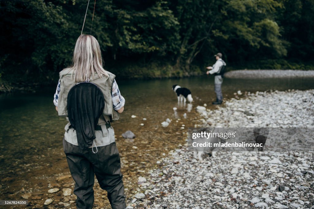 Pareja de adultos jóvenes está pescando juntos en el río de montaña rápida. Personas activas y concepto de pesca con mosca deportiva.