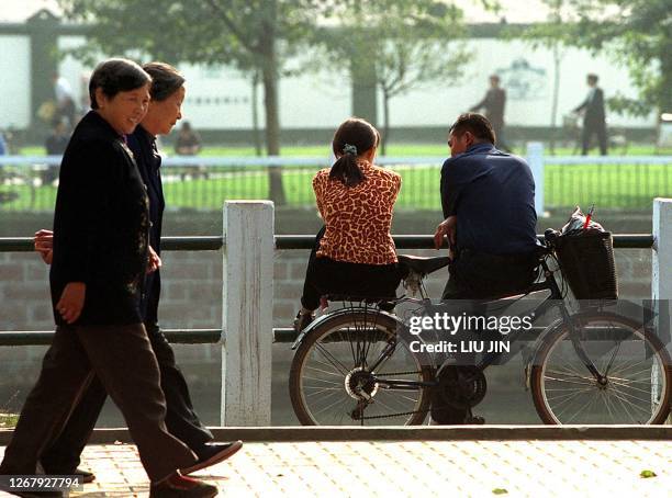 Two middle-aged women stroll past a young couple sitting on their bike next to the urban canal in Shanghai, 22 November 2000. AFP PHOTO/LIU Jin