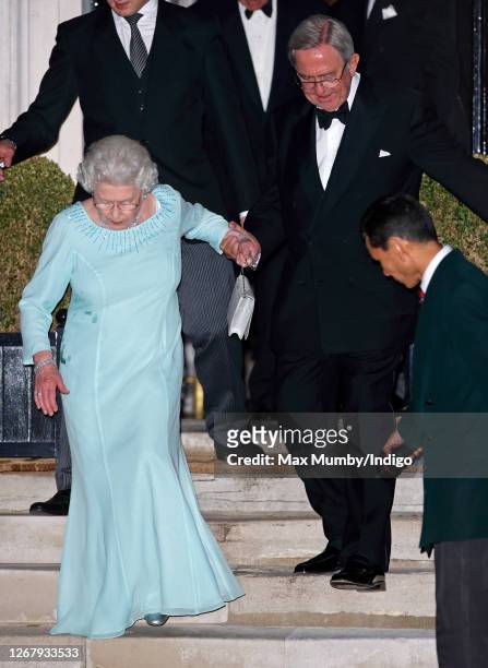 Queen Elizabeth II is helped down the stairs by King Constantine II of Greece after attending his 70th birthday party at Crown Prince Pavlos of...
