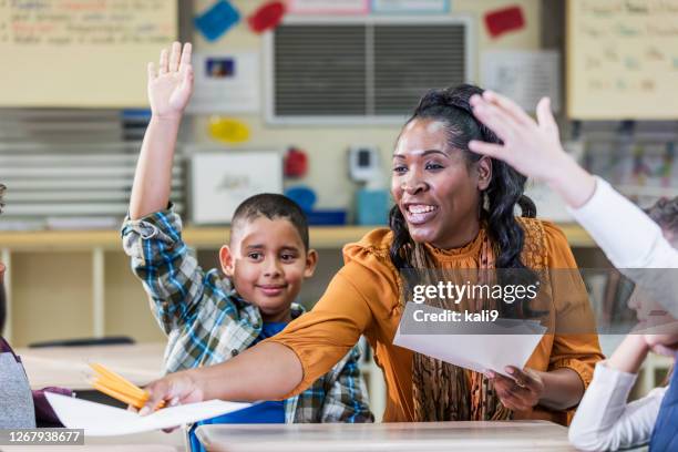 elementary school teacher handing out paper to students - grant writer stock pictures, royalty-free photos & images