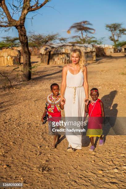 young caucasian woman walking with two african little girls - africa village stock pictures, royalty-free photos & images
