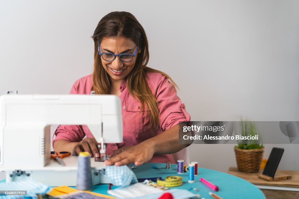 Woman working with sewing machine doing homemade medical face mask for preventing and stop corona virus spreading - Textile seamstress and healthcare people concept