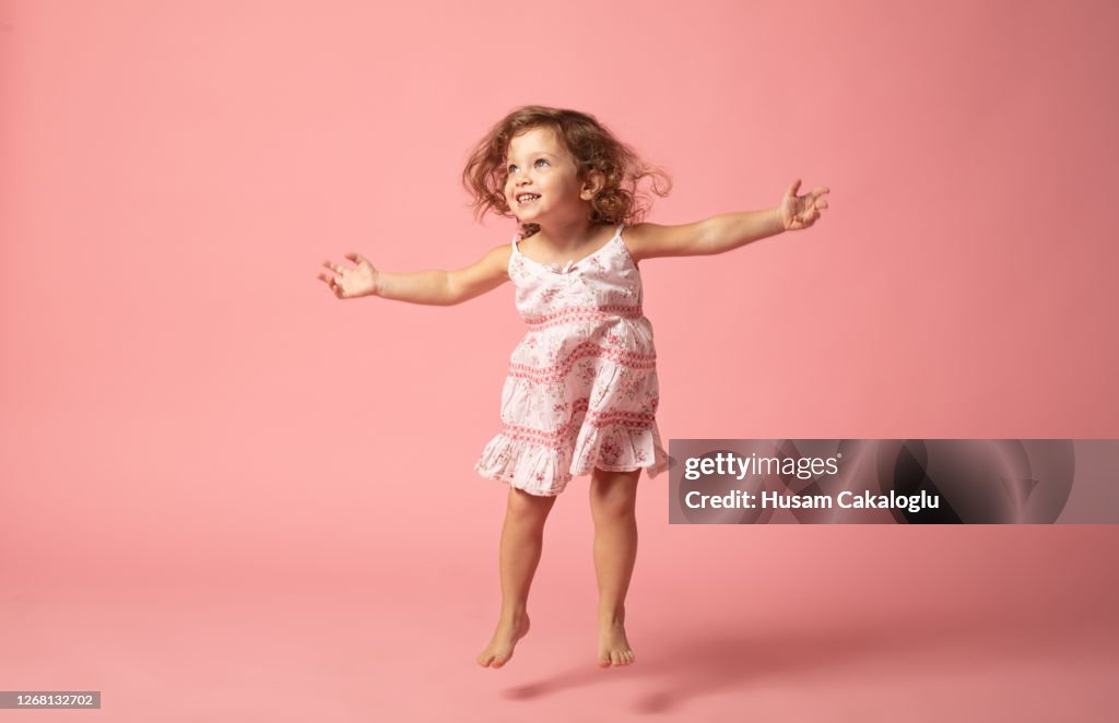 Linda niña con los pies descalzos saltando sobre el fondo rosa.