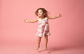 Cute baby girl with barefoot jumping on pink background.