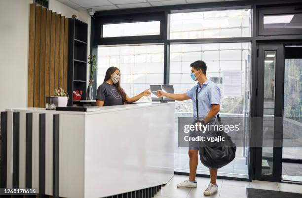 young man with face mask checking at gym and taking key - gym receptionist stock pictures, royalty-free photos & images