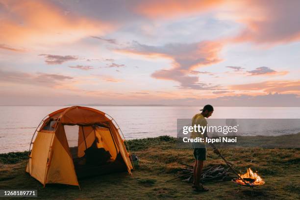 man with campfire and tent by the sea at sunset - japanese tents stock pictures, royalty-free photos & images