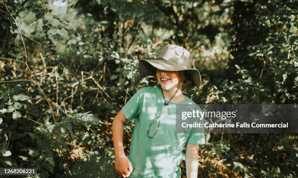 boy in a safari hat stands among trees in sun dappled surroundings - dappled sunlight stock pictures, royalty-free photos & images