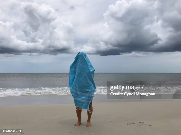 woman standing on the beach covered in a blanket - wrapped in a blanket stockfoto's en -beelden