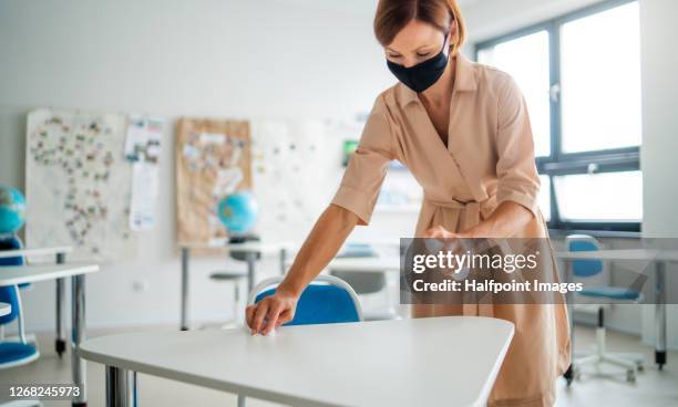 woman teacher with face mask disinfecting desks, back to school concept. - disinfection school stock pictures, royalty-free photos & images