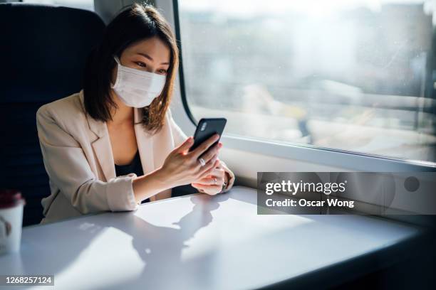 young woman sitting in train wearing protective mask, using smartphone - businesswoman mask stock pictures, royalty-free photos & images