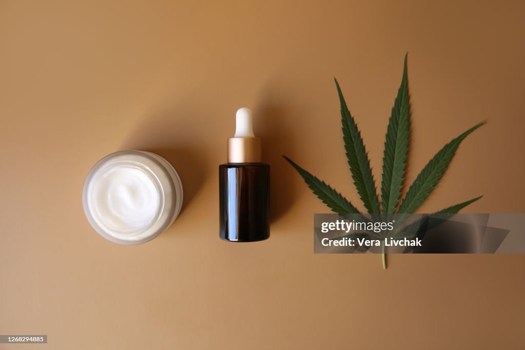 Bank of medicinal cream with CBD oil, bottle of cannabis oil, capsules, onbeige background. Flat lay, top view. Design, herbal.